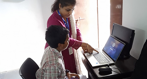 A lady teacher teaching a school boy pointing out something in the laptop