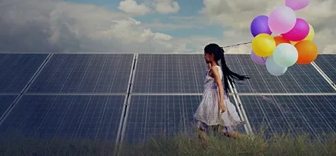 A girl running beside a solar grid holding a bunch of balloons in her hand