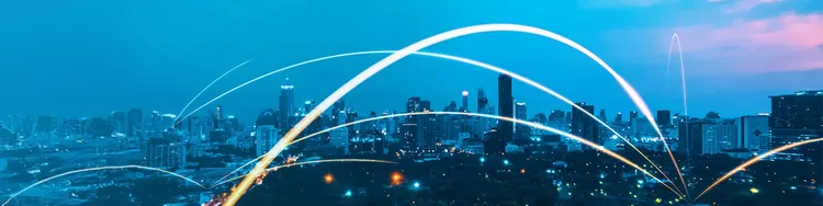 City skyline illuminated at night, featuring vibrant light trails weaving through the buildings.