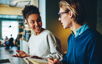 Two people interacting with each other in a library with books in hands