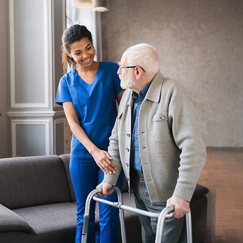 A nurse helping an elderly man walk using a walker.