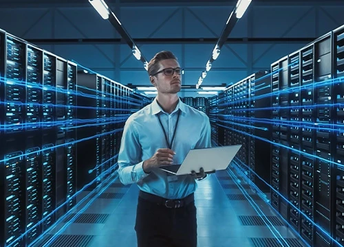 An engineer taking notes on a laptop inside a server room