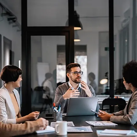 A man sitting at a table with an open laptop, in discussion with a group of people