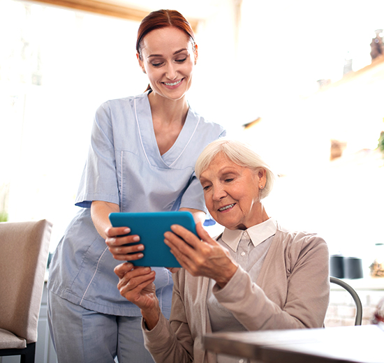 A lady nurse and elderly women both looking at a tablet