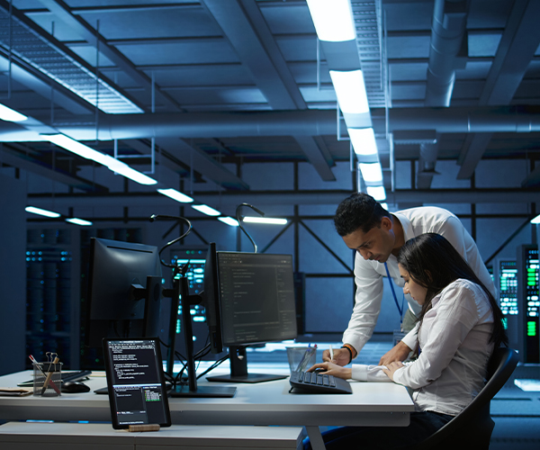 Two people collaborate in a modern server room with multiple monitors