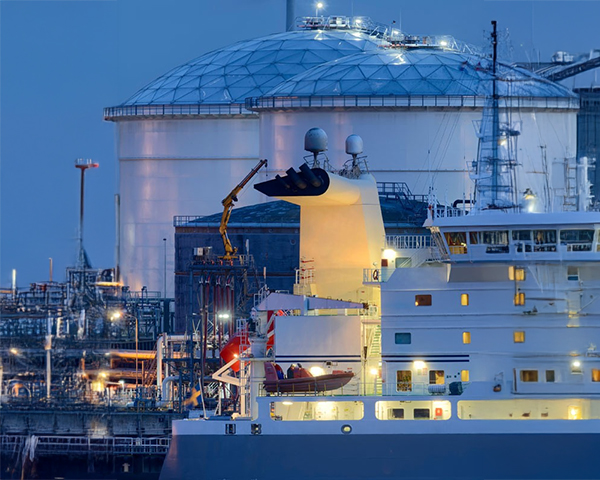 A large ship positioned in front of a sprawling oil refinery, showcasing industrial activity and maritime transport.