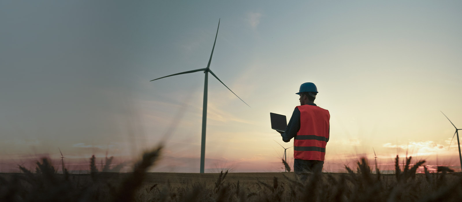 engineer standing in front of a windmill with a laptop in hand