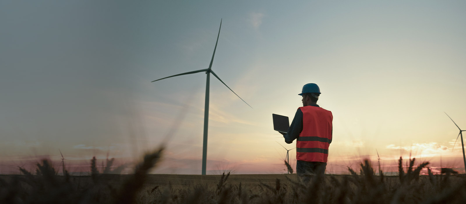 engineer standing in front of a windmill with a laptop in hand
