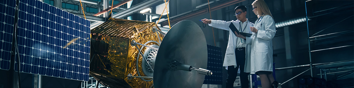 Two engineers inspecting a satellite under production