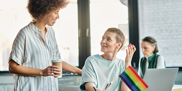 Two individuals engaged in conversation at a table adorned with a rainbow flag.