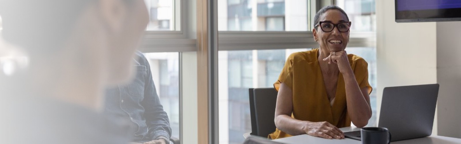 A lady sitting at a table with an open tablet, her chin resting on her fist, smiling and looking ahead