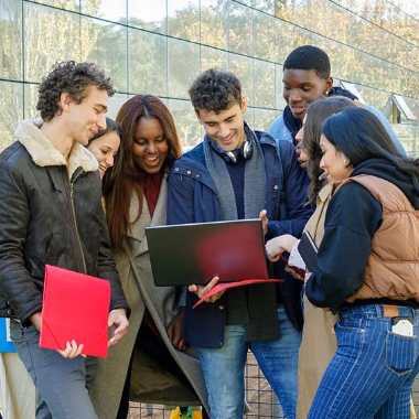 Diverse group of young men and women standing around a young man and looking at his laptop