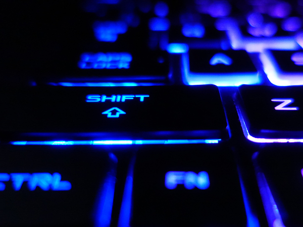  Close-up of illuminated blue keyboard keys, highlighting the Shift key in a dark, futuristic setting.