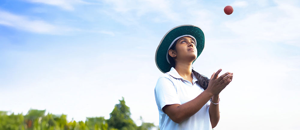 Girl wearing cricket uniform catching the ball on the field