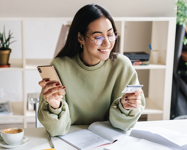 Person holding phone and card at desk with notebook coffee
