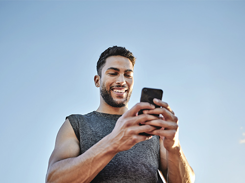 Male in grey sports top looking at mobile phone, smiling.