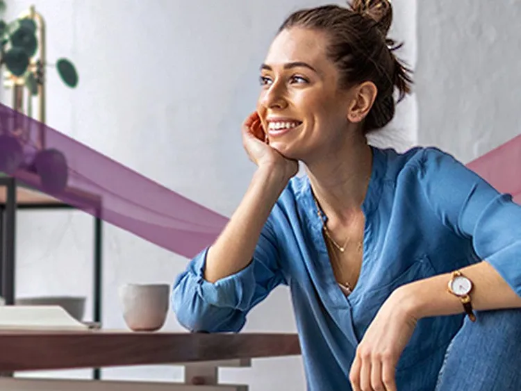 A woman is smiling while having a tea break in her workspace.