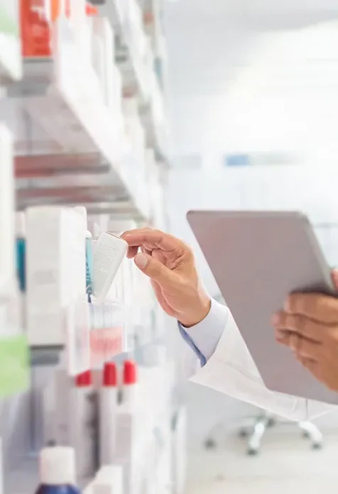 Closeup view of healthcare professional holding a tablet with one hand and choosing medicine from shelf with the other hand