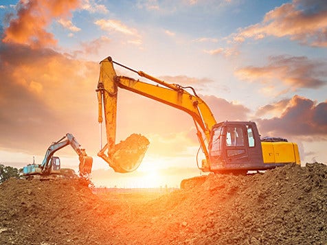 A yellow excavator is actively digging into a pile of dirt at a construction site.