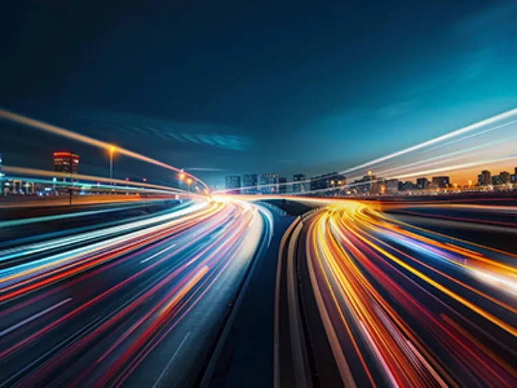 A highway at night with blurred traffic, indicating high speed motion