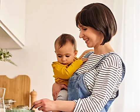 A woman holding a baby and stirring food in a bowl