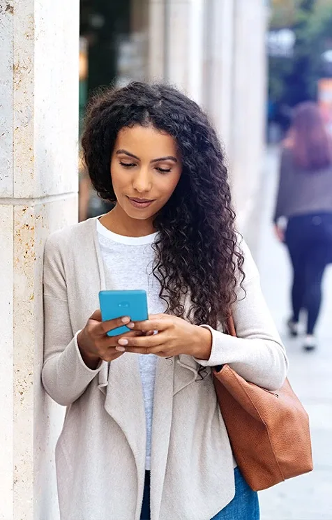 A girl leaning on a column outdoors and using her mobile phone