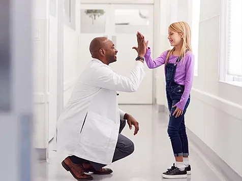 A child standing and giving high-five to doctor who is down on his haunches