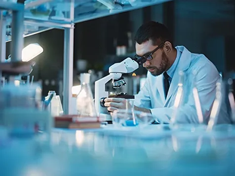 A lab technician peering into a microscope