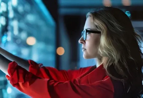 A woman wearing a red shirt, standing and itneracting with a digital glass screen