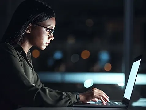 A woman wearing glasses types on a laptop, focused on her work.