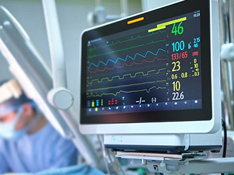 A screen showing line graphs while surgeons are at work in an operting theater