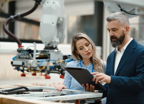 Two professionals reviewing a tablet beside an industrial robot.