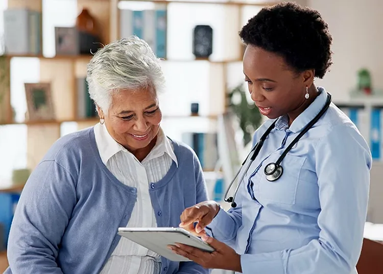 A doctor wearing a stethoscope pointing at a tablet to an elderly smiling patient