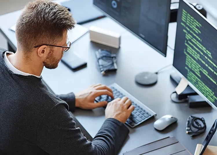 A man sitting at a computer table and typing on a keyboard in front of a monitor