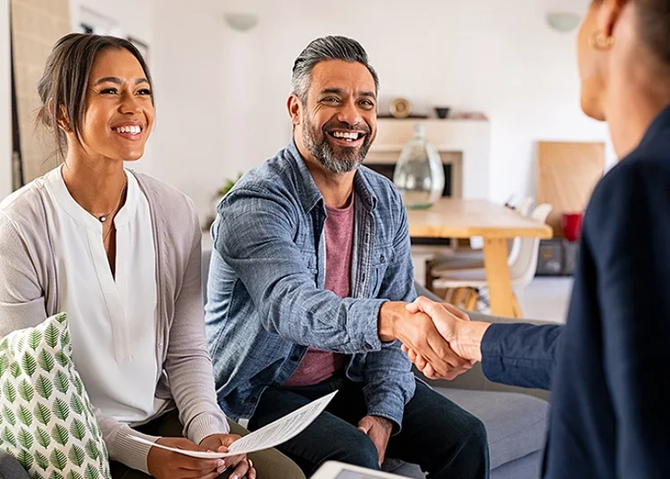 A smiling couple sitting on a sofa and the man shaking his hand with a professional sitting across