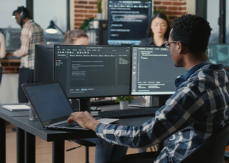 A person looking into multiple desktop monitors and a laptop at work