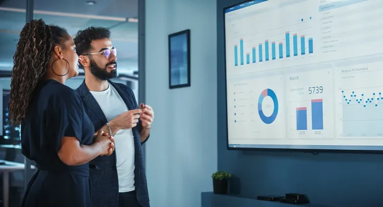 Two people examining a screen filled with graphs and charts