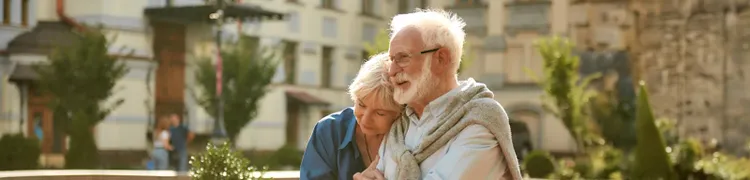 A senior couple walks hand in hand along a city sidewalk