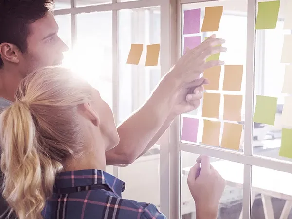 A man and woman examine colorful sticky notes arranged on a wall