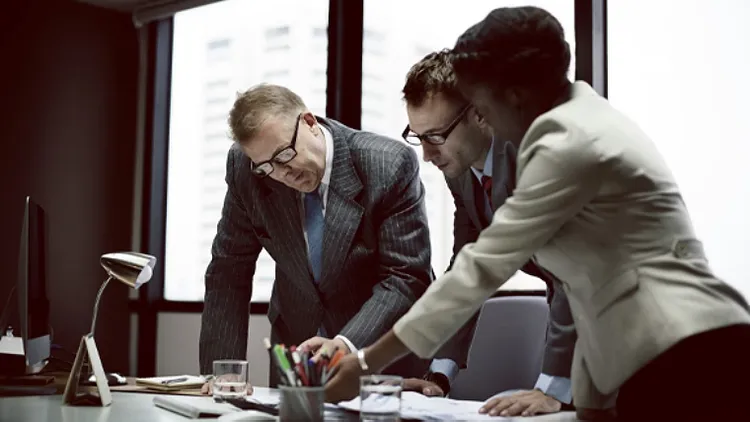 Three colleagues standing at a table and focussing on some documents