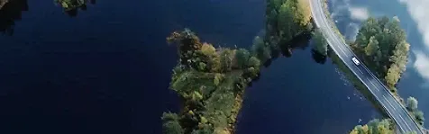 A solitary white car on a road between two waterbodies