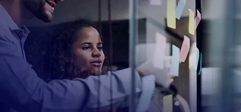 A man and woman sticking sticky notes to a glass wall.