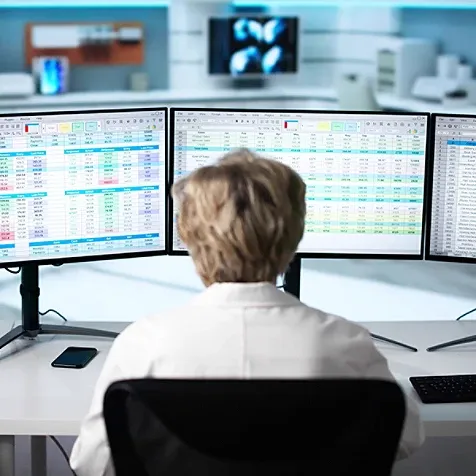 View from behind a female healthcare worker looking at data on her monitor screens.