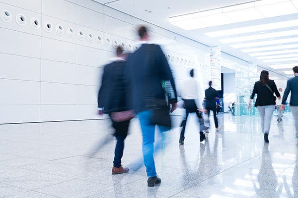 A diverse group of people walking together inside a spacious building with high ceilings and large windows.