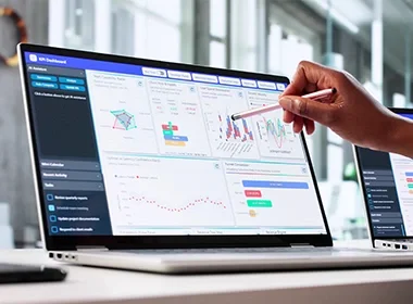 Hand using stylus on laptop with analytics dashboards