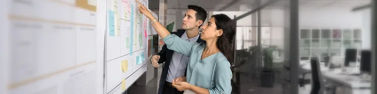 A woman pointing to a whiteboard to a male colleague