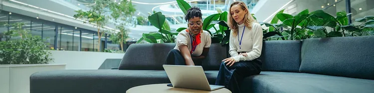 Two women sitting on a couch, focused on a laptop, engaged in conversation and sharing ideas.