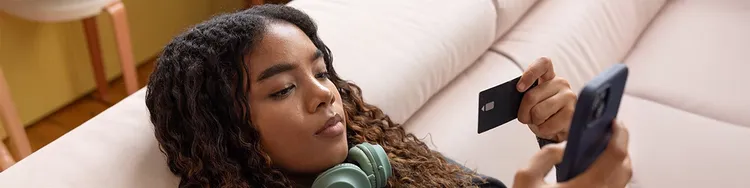 A woman relaxes on a couch, wearing headphones and using a cell phone, enjoying her leisure time.