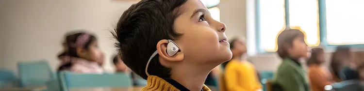 In a classroom, a child with headphones is engaged in learning at their desk.