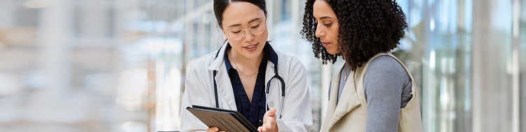 Healthcare professional showing tablet information to person in modern hallway